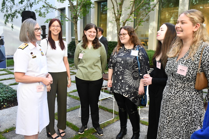 A woman in a Rear Admiral white uniform talking with five younger women.