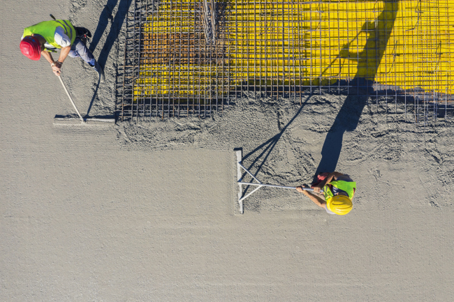 Two builders seen from above smoothing out a big patch of concrete with rebar inside it.